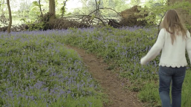 Woman walking and jumps pathway through bluebell woodland shot wide shot