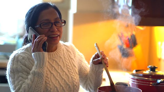 Hispanic woman in kitchen cooking and talking in cell phone
