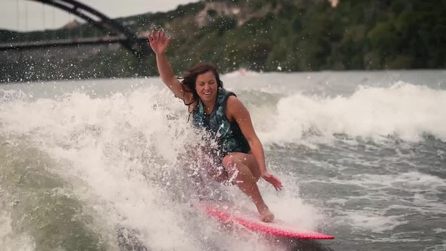 Wake surf professional does slow motion ollie behind boat with pennybacker bridge in the background on Lake Austin, Texas