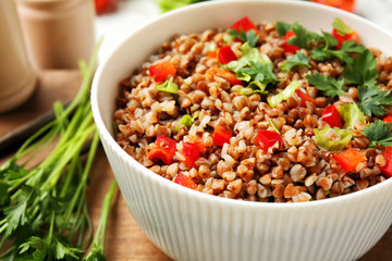 Bowl of tasty buckwheat porridge and vegetables on table, closeup