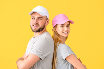 Young couple in stylish caps on color background
