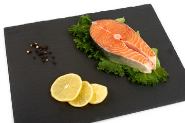 fresh salmon steak on a slate plate with lemon , isolated on a white background.