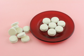 Mini cookies dipped in white fudge on small red dessert plate and heap on pink background