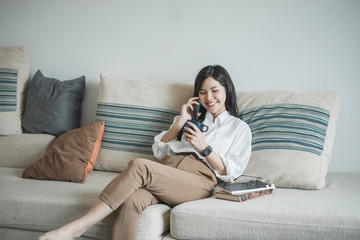 Pretty young asian women talking on the phone and holding coffee on the sofa at home.