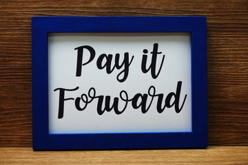 Pay It Forward written with blue photo frame on wooden background