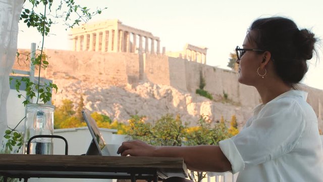 Young woman using laptop on home balcony with view on Parthenon, Acropolis of Athens, Greece. Working from home.
