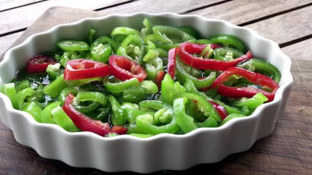 Green and red pepper salad in white plate on wooden surface.