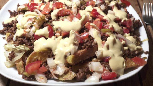 Zoom to loaded fries with colorful toppings and white sauce on it.