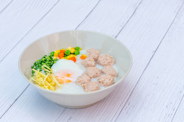 Delicious Thai Hong Kong Style Congee mixed with pork, meat, and Soft-boiled eggs in the round bowl on the white wood background. Thai, Hong Kong breakfast.