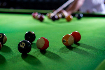 Man's hand and Cue arm playing snooker game or preparing aiming to shoot pool balls on a green billiard table. Colorful snooker balls on green frieze.