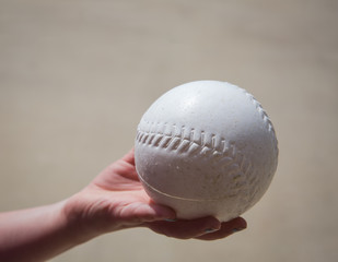 Child's hand holding a white plastic baseball