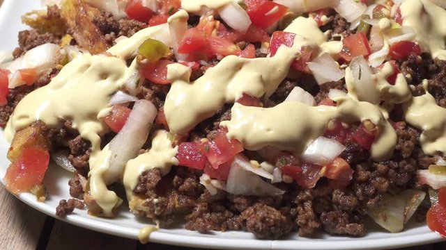 Panning on loaded fries with colorful toppings and sauce.