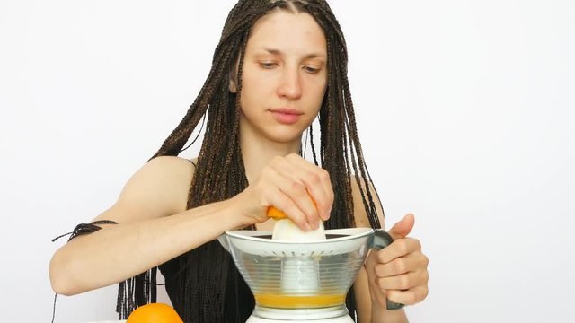 A young beautiful lady with zizi braids makes orange juice and drink it from a glass against white background
