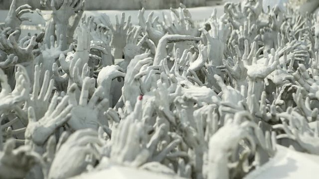 Panning shot of white hand sculptures at famous Buddhist temple on sunny day - Chiang Rai, Thailand