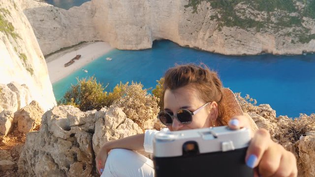 Young woman at Navagio Beach Shipwreck in Zante., taking selfies with vintage camera. Lagoon of Zakynthos island, Ionian Sea, Greece