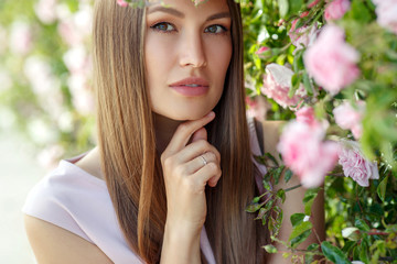 Beautiful young woman in nature in roses. Brunette girl with roses.