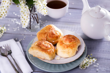 sweet buns on ceramic plate, blossom branches on white wooden background