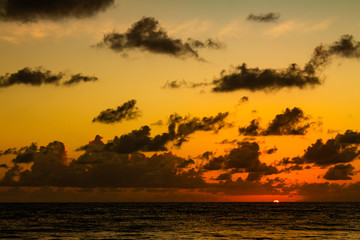 Fototapeta na wymiar Beautiful sunrise on the ocean. The sun appears on the horizon line with the sky with beautiful colored clouds.