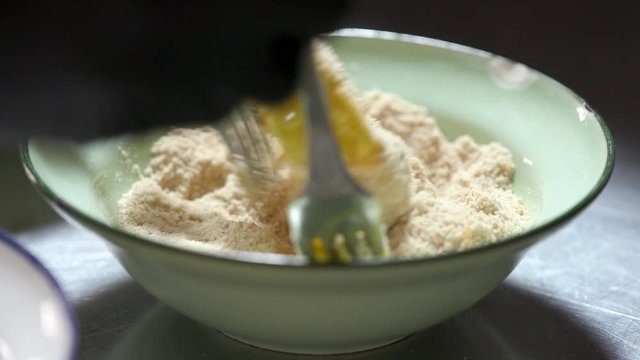 Someone making a healthy cod or stockfish patty. Hands with gloves on the fresh fish with flour and eggs, put into the bowl with bread crumbs, preparing to fry it.