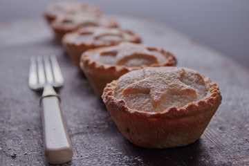 Row of mince pies that have been dusted with icing sugar,they are resting on a wooden bench.
