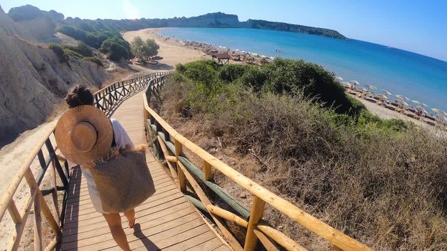 Young woman walking towards Zante beach on wooden walkway, Zakynthos island, Greece.