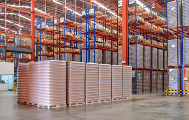 Pallets of empty plastic glass stack in a shorting area inside a distribution warehouse.