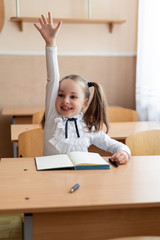 Naklejka premium girl schoolgirl sits at a lesson at her desk. He pulls his hand very strongly up.