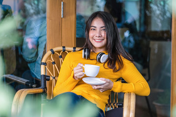 Asian young female holding a cup of coffee and sitting in modern coffee shop or coworking space