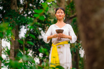 mind and body connection - beautiful and happy healer Asian woman holding incense cup doing ritual traditional healing dance at green tropical forest in wellness
