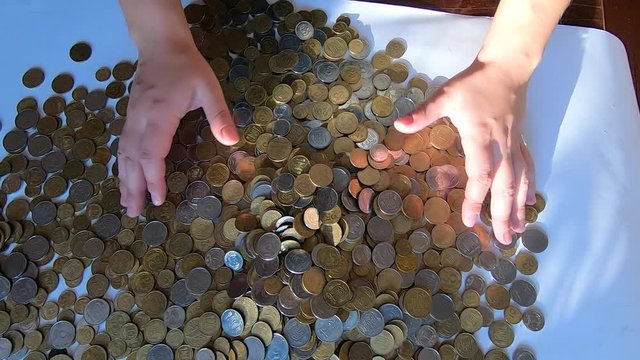 Person two hands rakes coins on table and pours spills from handful to surface
