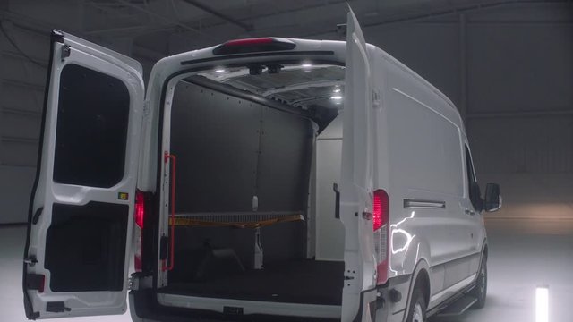 Track around rear of white cargo vans in an empty warehouse with its rear doors open
