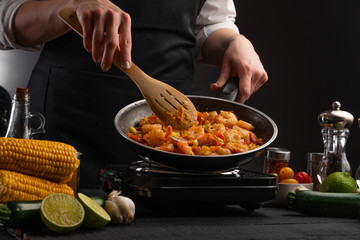 Chef fries shrimps in a pan with vegetables. On a gray background, cooking and recipe book. Seafood