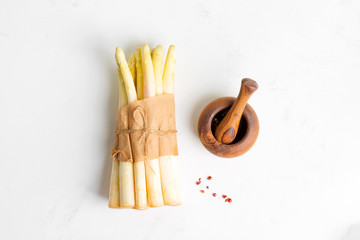 Bunch of freshly picked raw organic white asparagus and wooden mortar with paper on a light grey stone background.