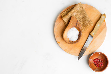 Wooden board with natural salt and red paper in a small bowl for cooking fresh delicious food on a light grey marble background.