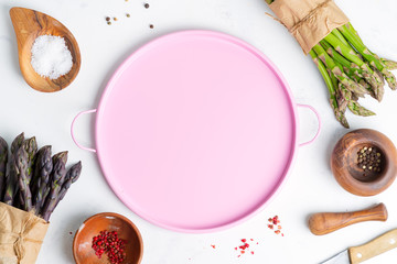Top view of cook background with bunches of fresh natural organic asparagus vegetables with different condiments and pink plate.