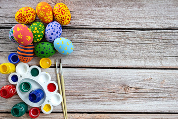 Pile of painted ester eggs in various colors and with brush and paint on wooden table. Ester holiday concept.