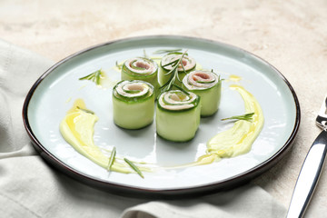 Plate with tasty cucumber rolls on light background