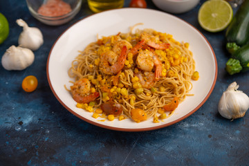 Fried prawns with vegetables and noodles, spaghetti. On a blue background
