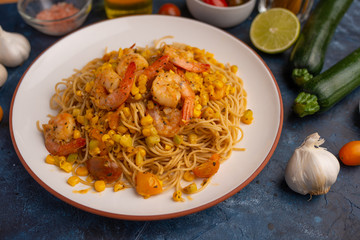 Fried prawns with vegetables and noodles, spaghetti. On a blue background