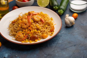 Fried prawns with vegetables and noodles, spaghetti. On a blue background