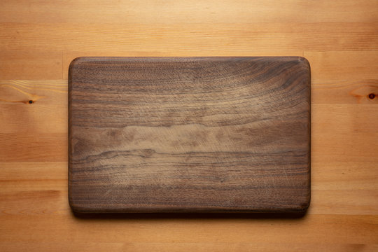 Handmade black walnut wooden chopping board with traces of knife carving on the table. Cutting board on wooden background.