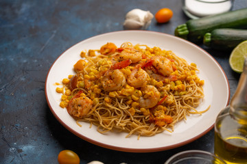 Fried prawns with vegetables and noodles, spaghetti. On a blue background