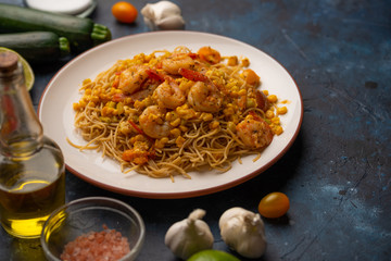 Fried prawns with vegetables and noodles, spaghetti. On a blue background