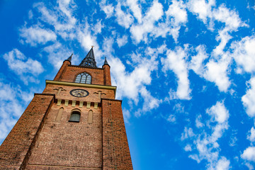 Fototapeta na wymiar The Tall Steeple of the Riddarholmen Church Offset Left with a Cloudy Blue Sky behind It in Stockholm, Sweden