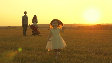 Happy child and parents walk at sunset. Dad hugs daughter and whirls in flight. Silhouette of a family walking in the sun. Mom dad and baby. The concept of a happy family. Family lifestyle.