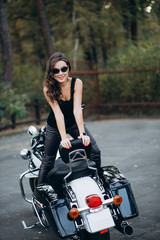 Fototapeta na wymiar Young beautiful biker woman in glasses with a black tank top and leather pants on a motorcycle. The concept of speed and freedom. Soft sective focus.