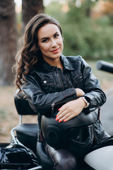 Young beautiful biker woman in a black leather jacket on a motorcycle with a helmet in his hands. The concept of speed and freedom. Soft selective focus.