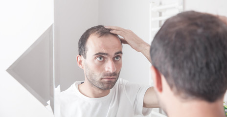 Fototapeta premium Caucasian man looking hair near mirror. Hair loss