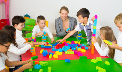 Teacher and happy schoolkids playing building blocks