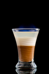 coffee cream alcoholic cocktail B52 in three layers was set on fire and burns with a blue flame in a shot glass on a black background
